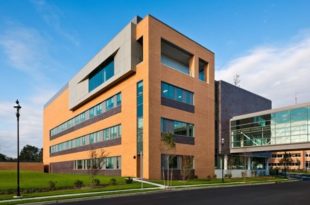 This image depicts Shore Memorial Hospital. It is a four-story building beside a black asphalt road. It features Mapes impact-resistant panels.